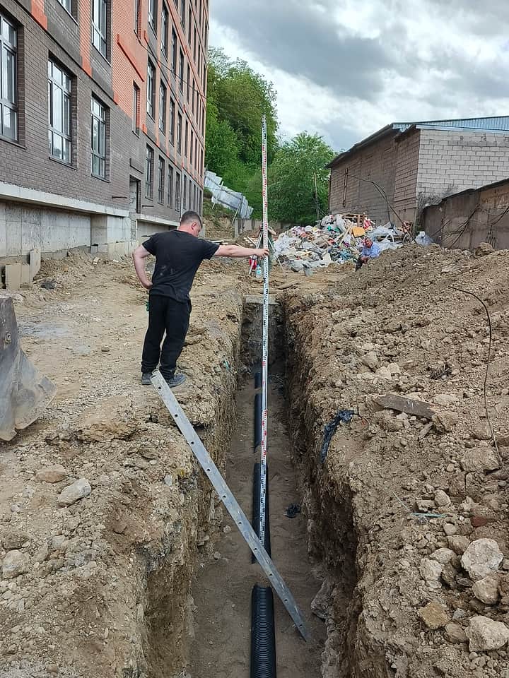 Проверка уровня при укладке труб у дома